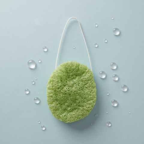 Green exfoliating pad on a light blue background with water droplets
