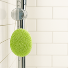 Green sponge hanging on a shower handle against a tiled bathroom wall.